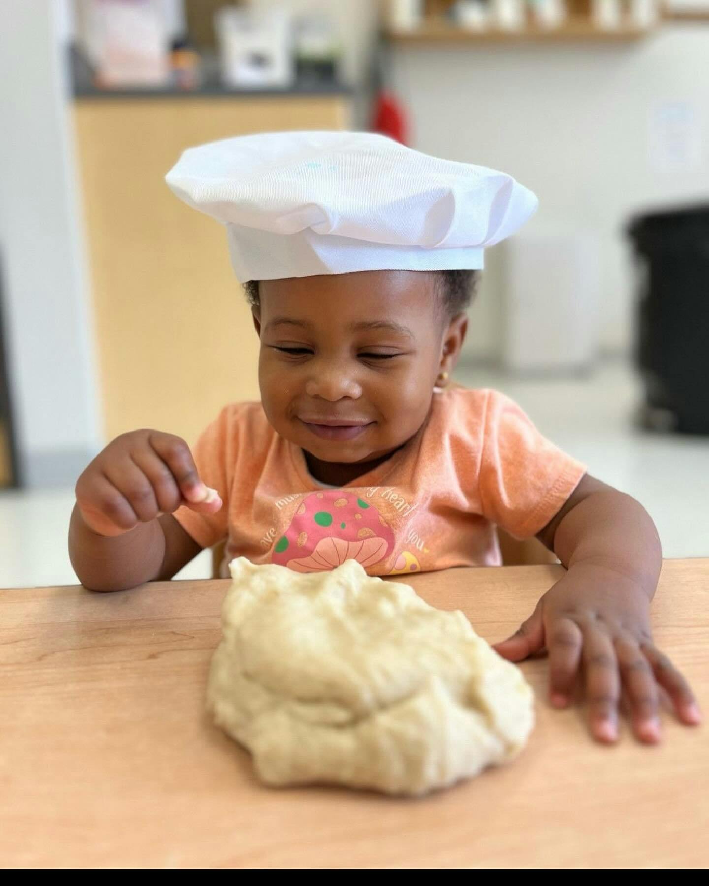 Child in chef hat with dough on a table