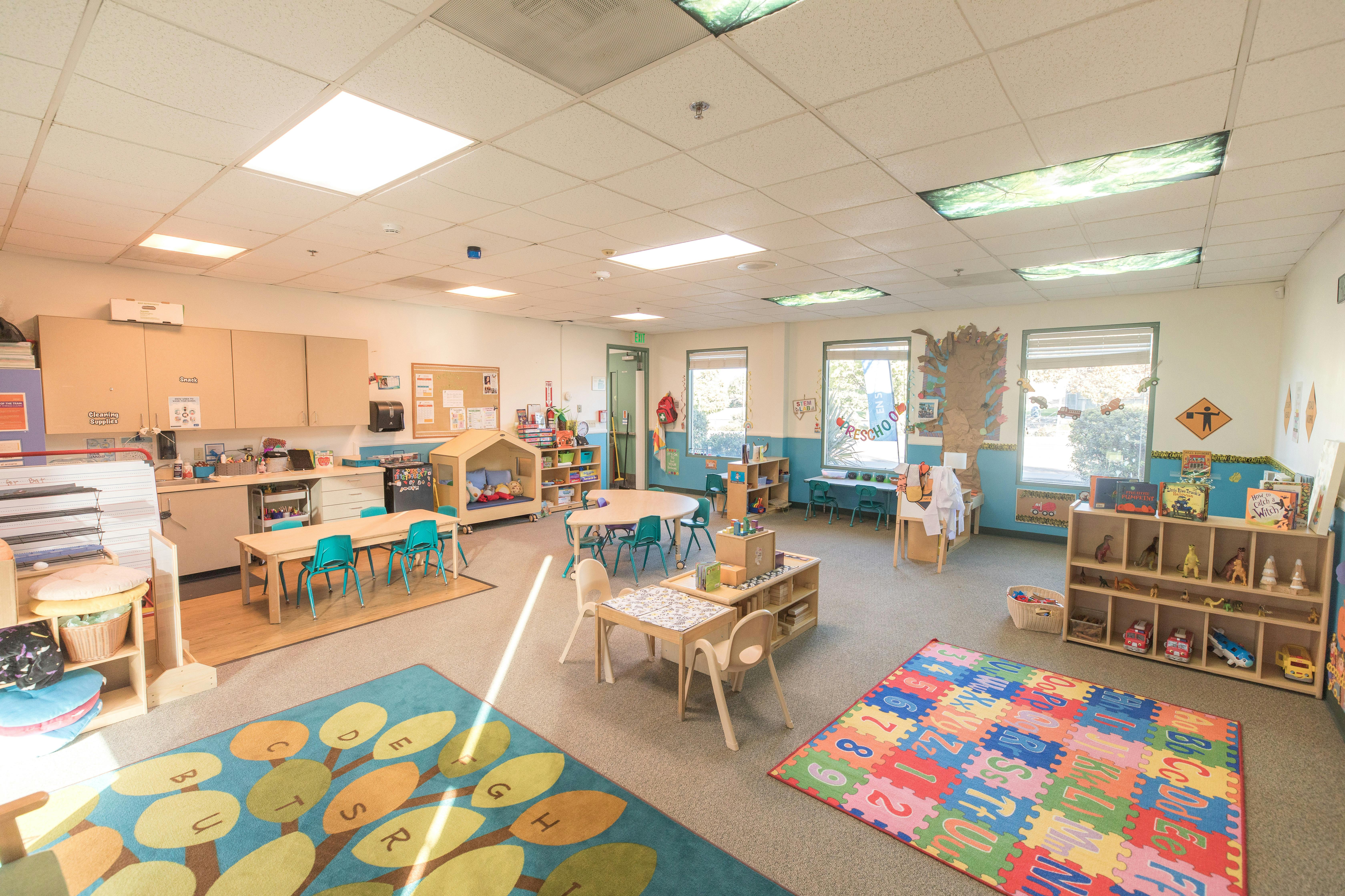 Empty classroom with small tables, chairs, and colorful rugs