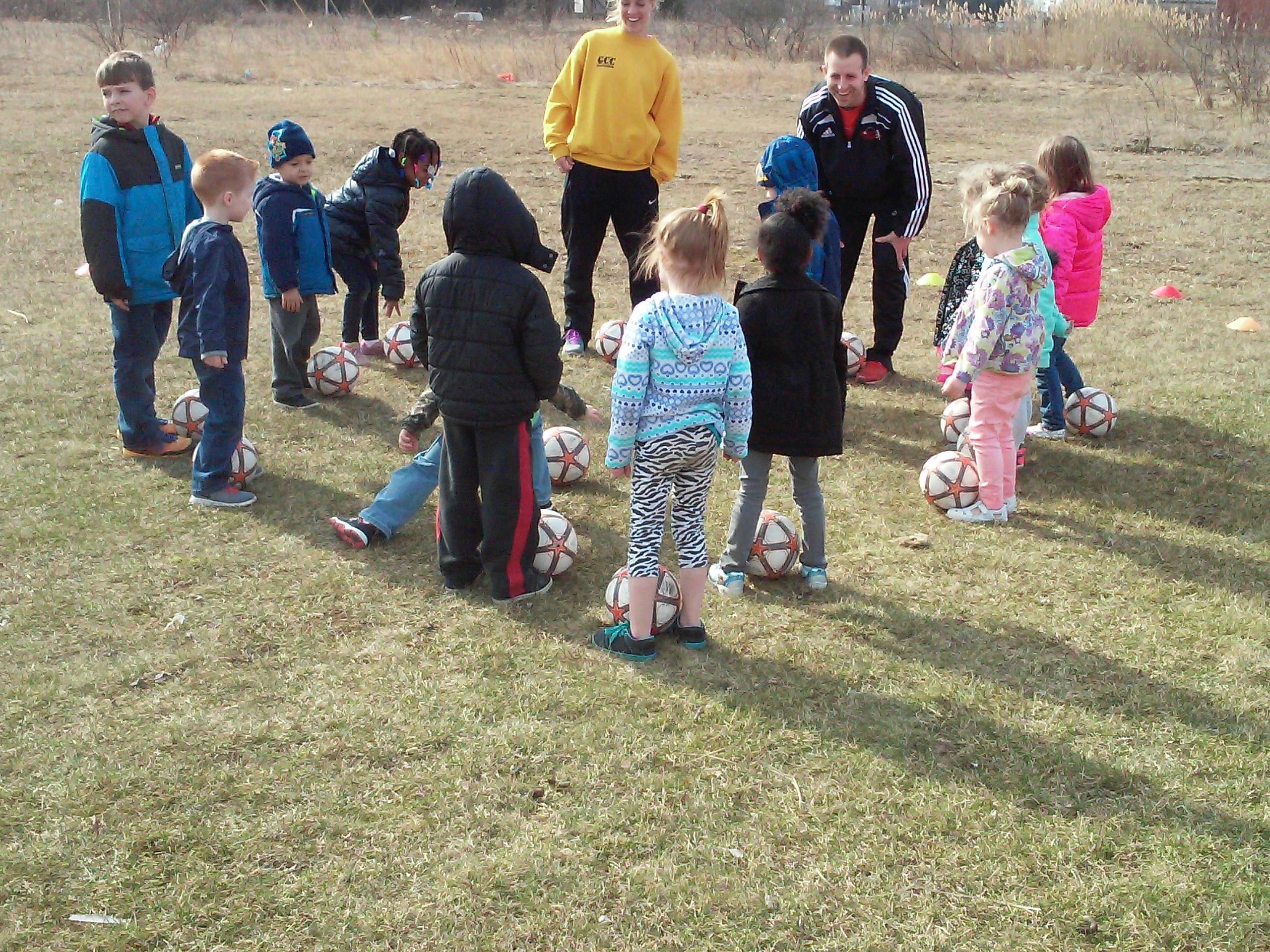 Adults and children on a grassy field with soccer balls