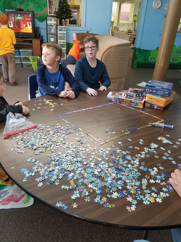 Children sitting around a table with puzzle pieces scattered across it