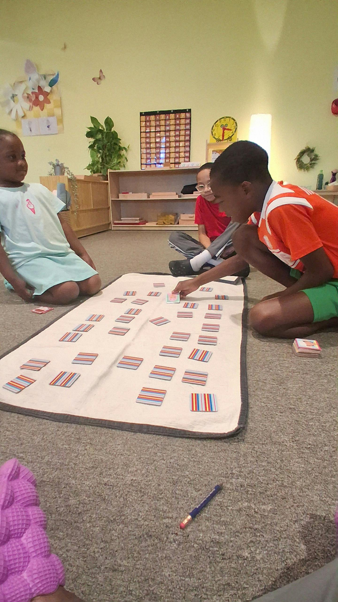 Three children playing a card game on a mat in a classroom