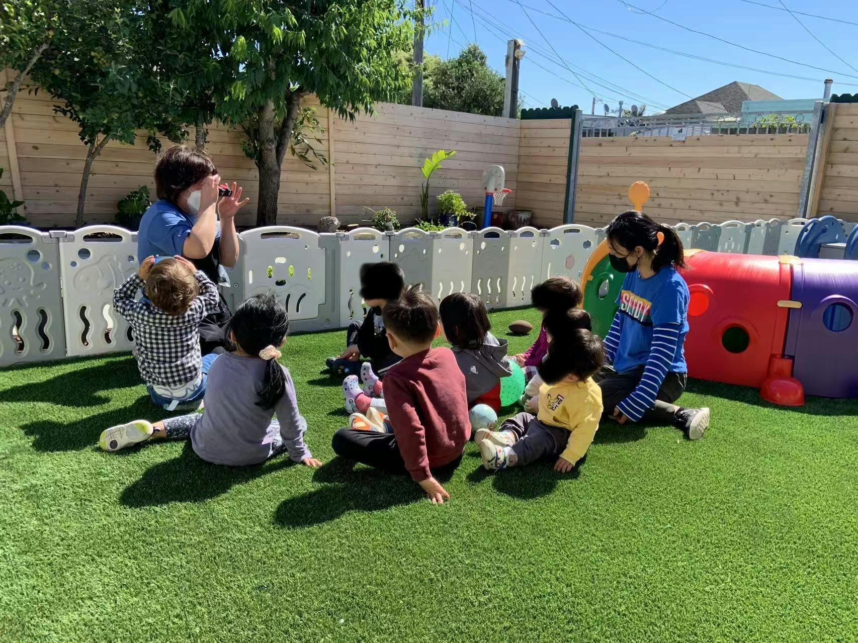 Adults and children sitting on grass in an outdoor play area