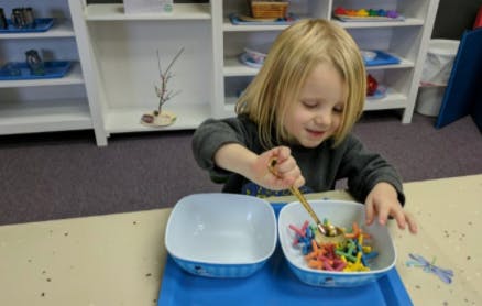 Child using a spoon to transfer small objects between bowls