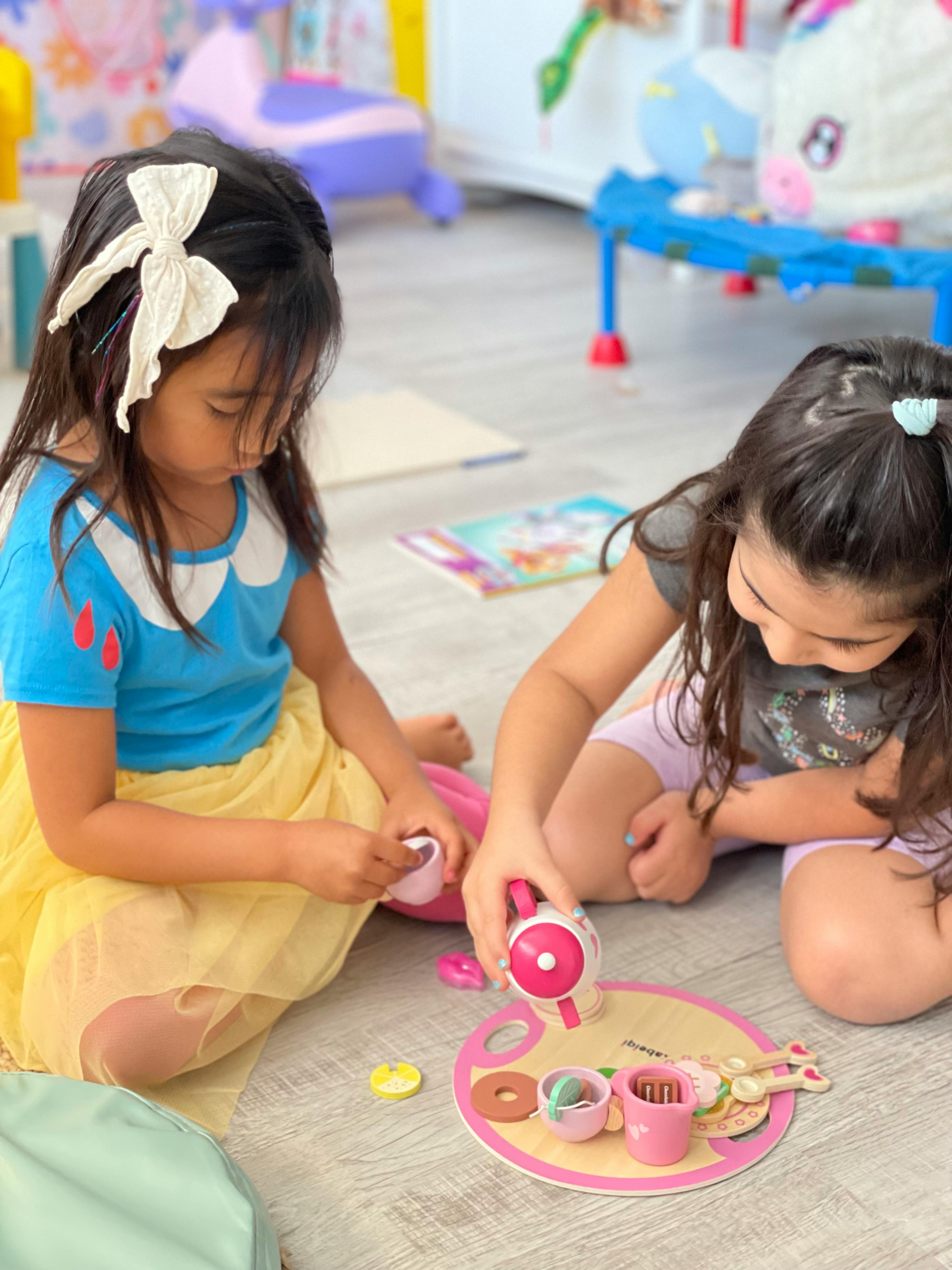 Two children playing with a toy tea set on the floor