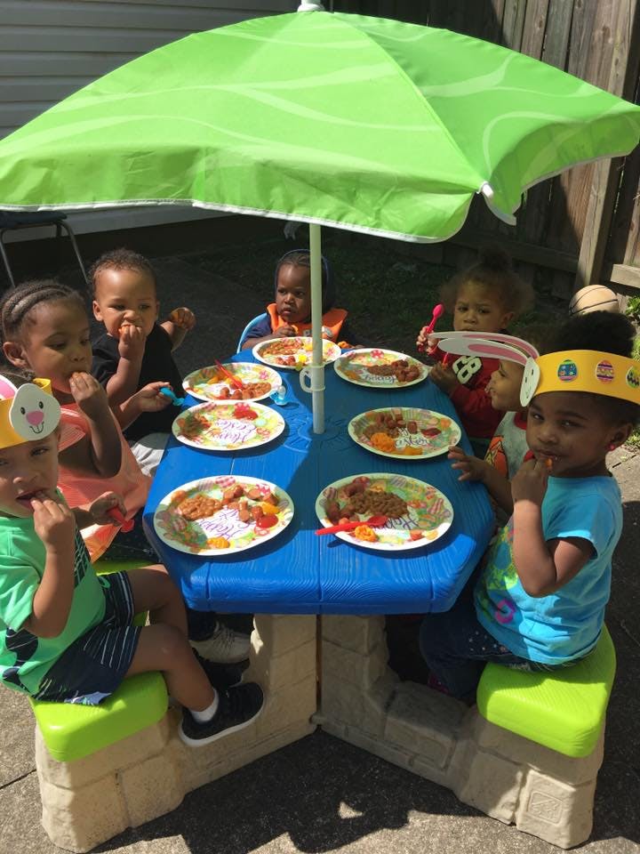 Children eating at a picnic table under a green umbrella
