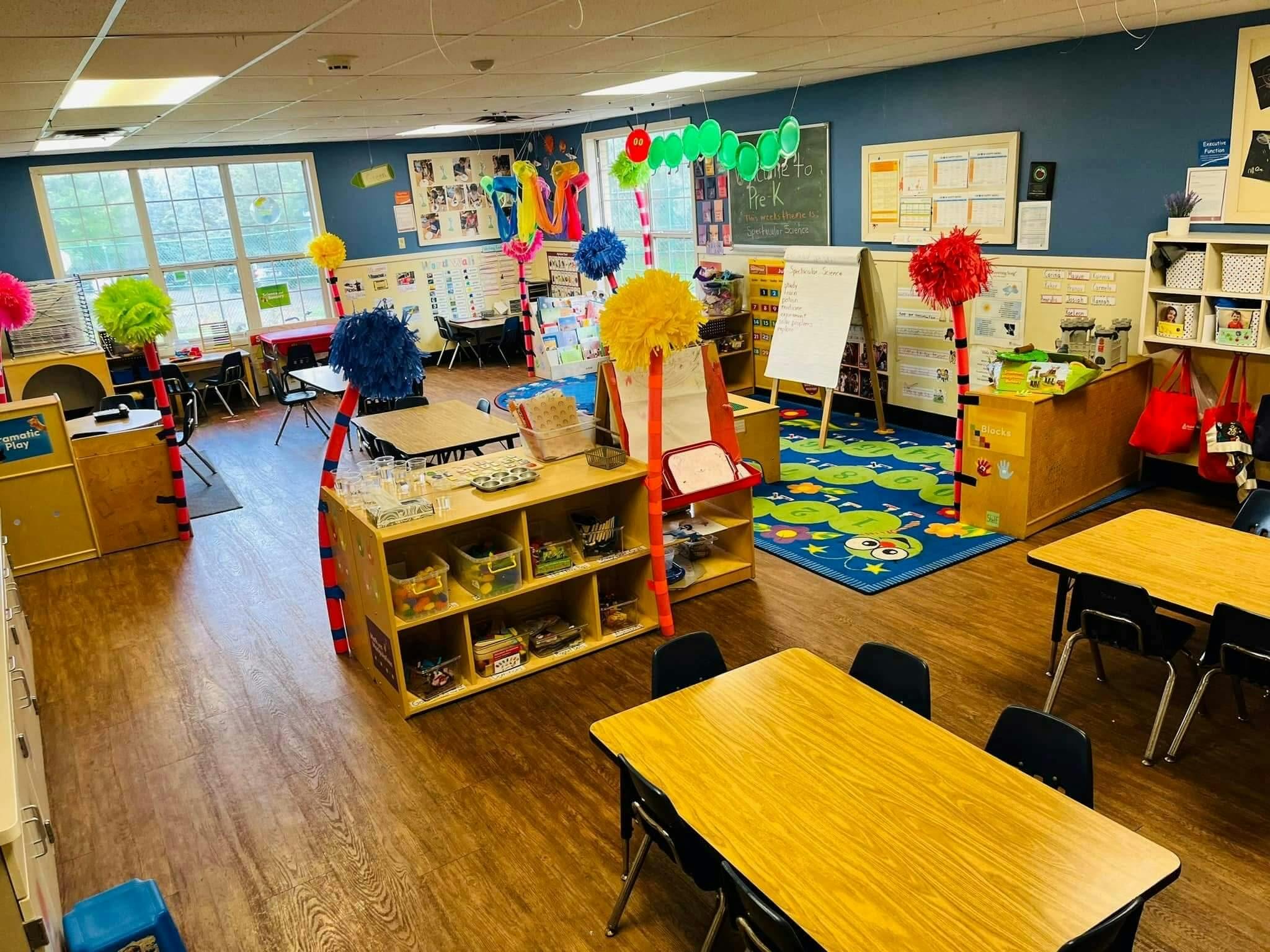 Classroom with child-sized tables and chairs, shelves, and a colorful rug