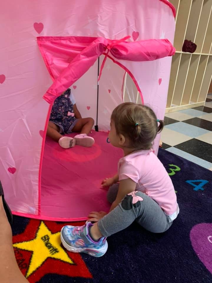Child sitting outside a pink play tent with another child inside