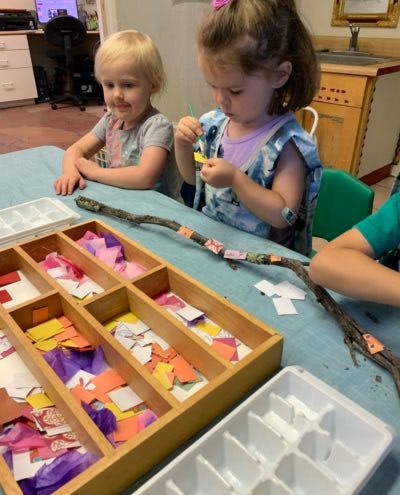 Two children decorating a stick with small pieces of paper