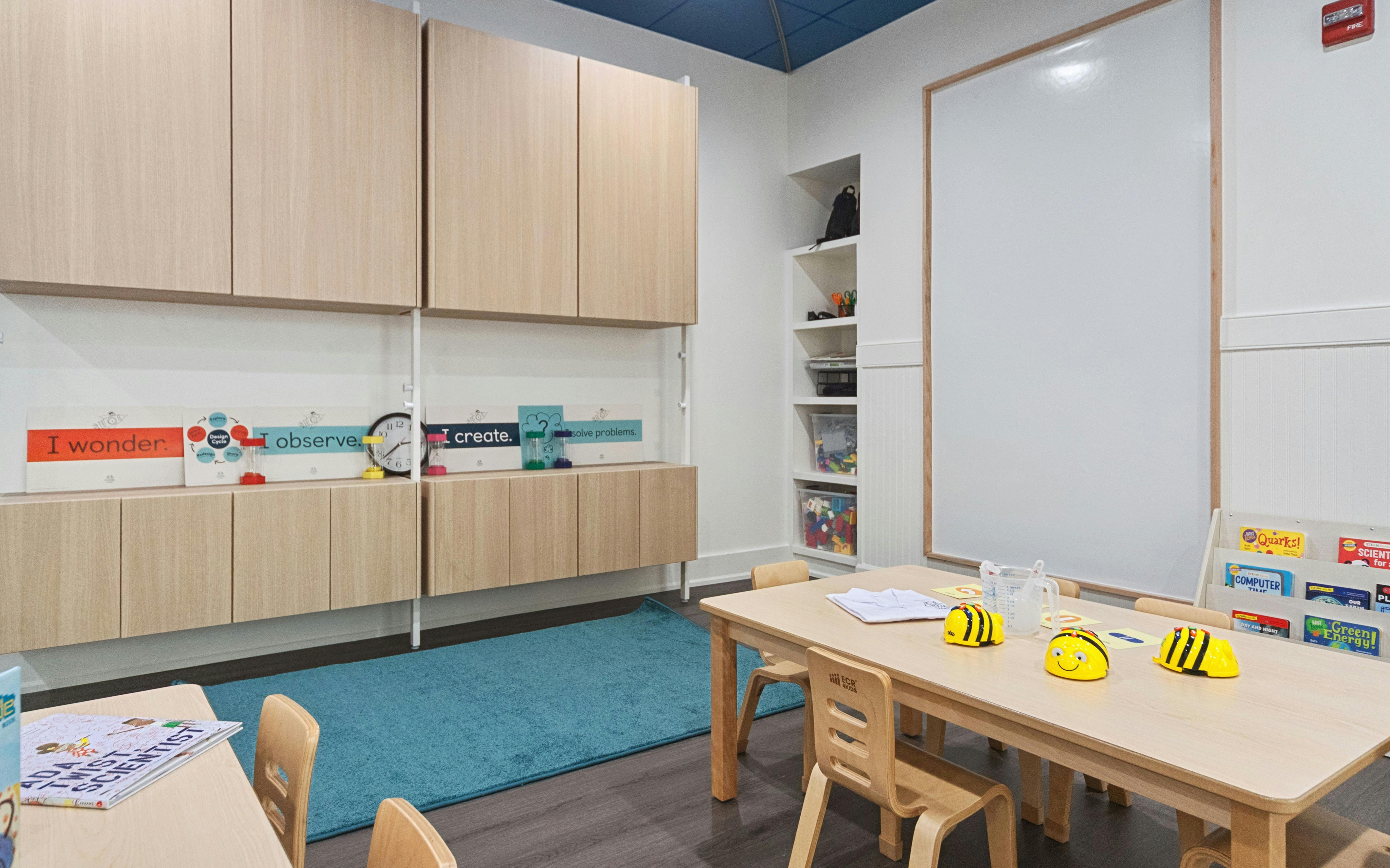 Classroom with wooden cabinets, a whiteboard, and tables with toy bees