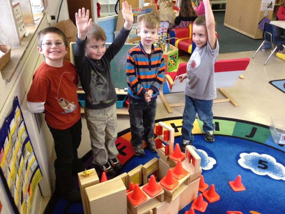Four children raising their hands in a classroom