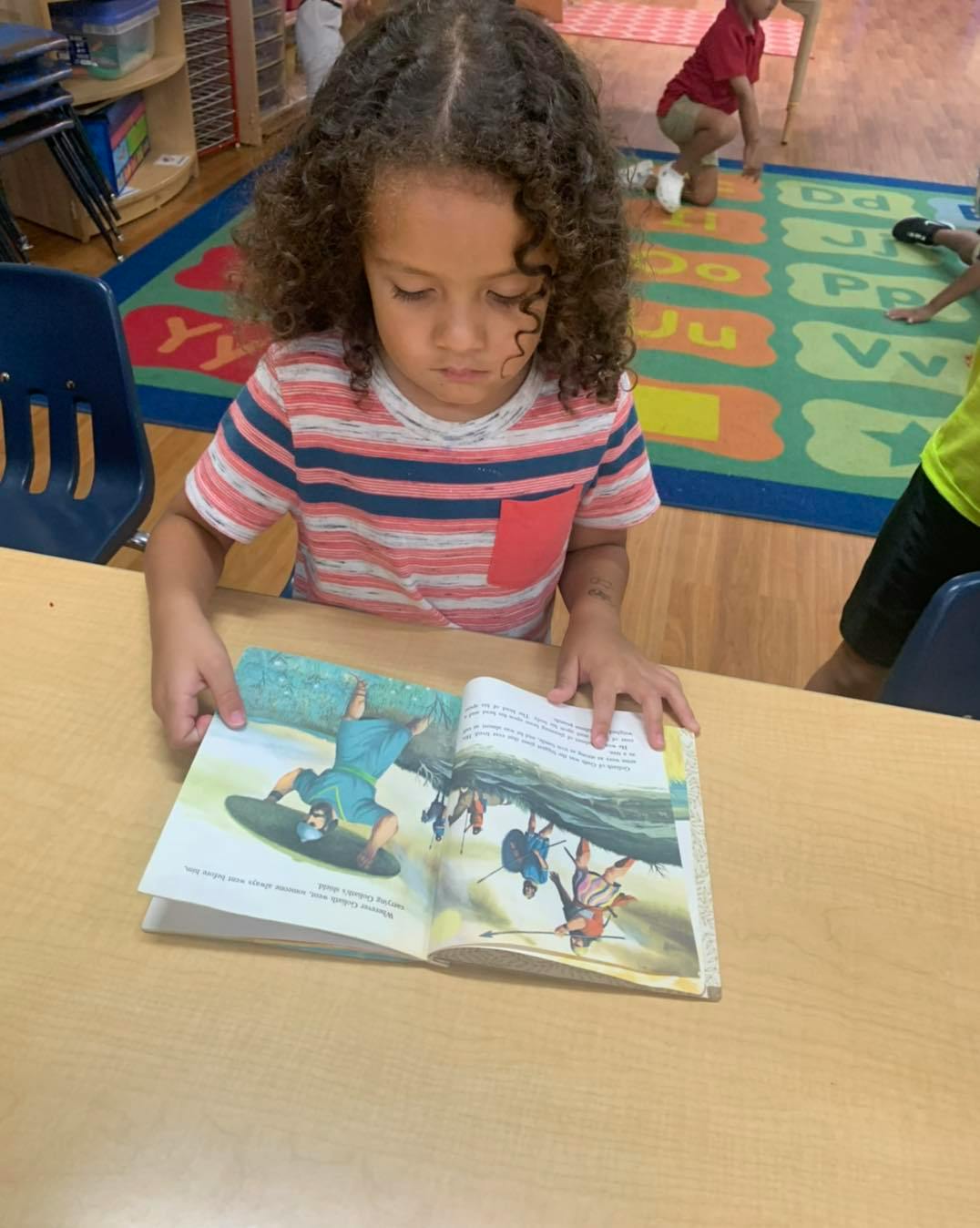 Child with curly hair looking at an open book on a table