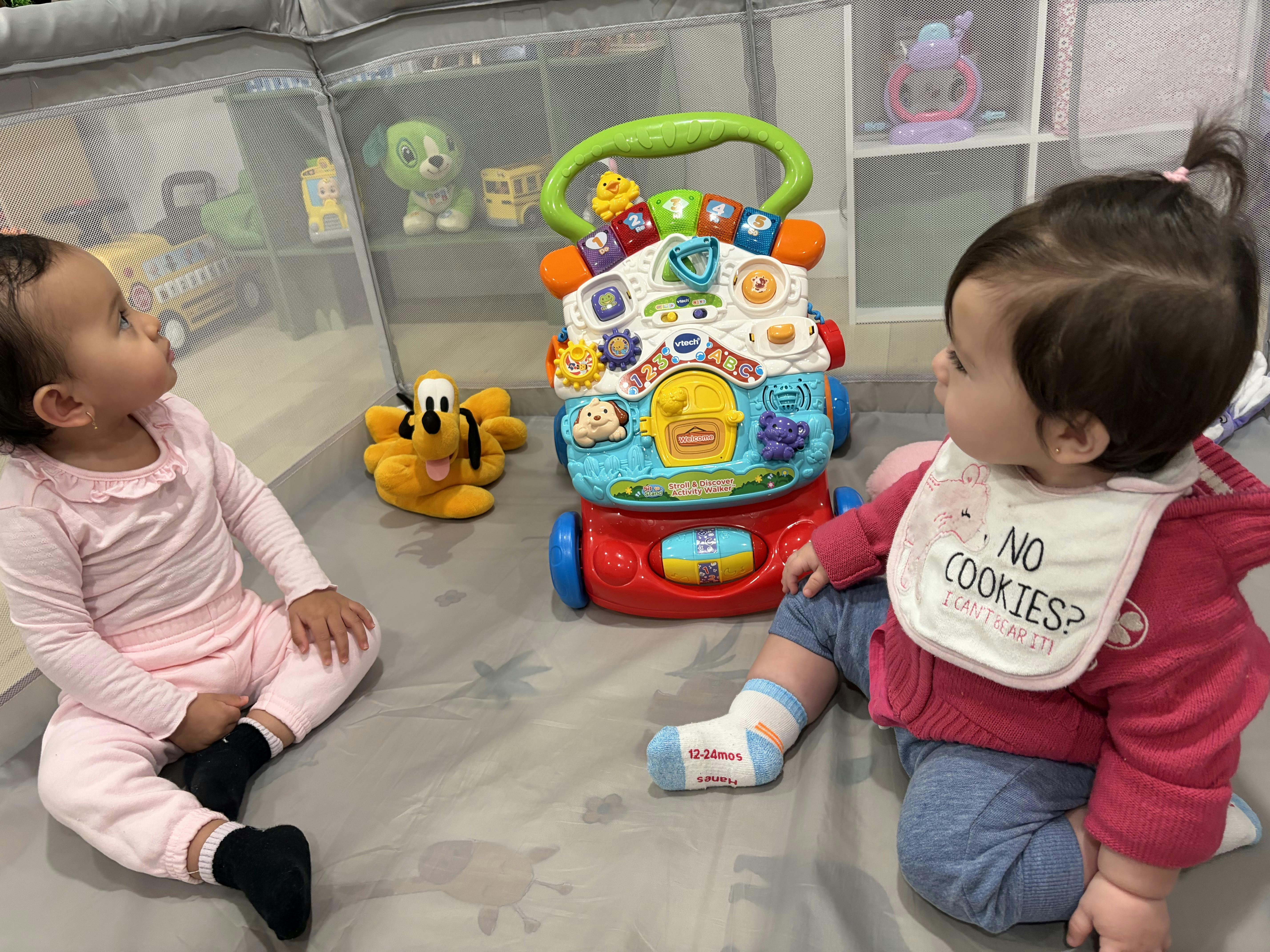 Two children sitting on the floor with a toy walker and a stuffed animal