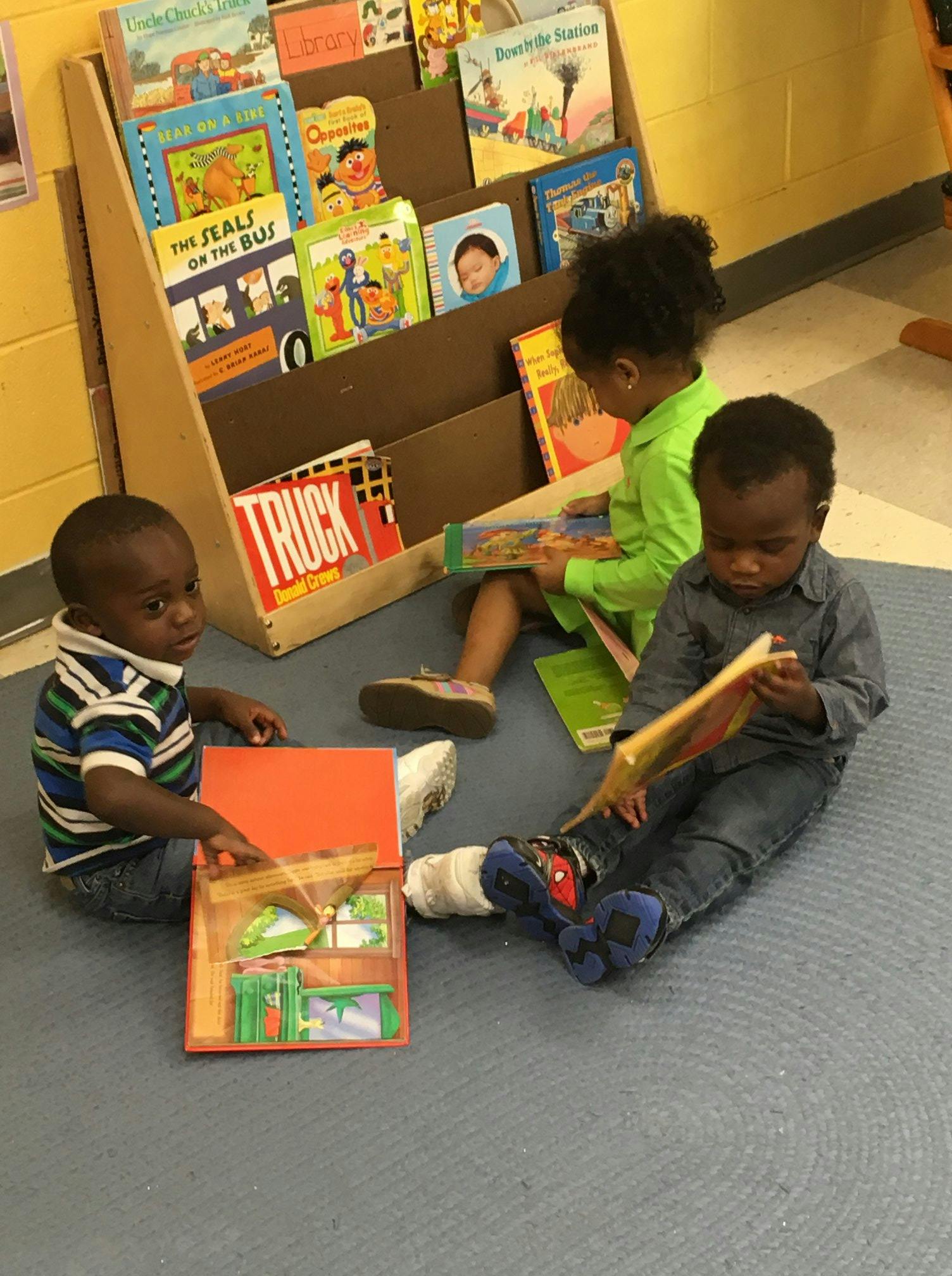 Three children sitting on the floor reading books in a classroom