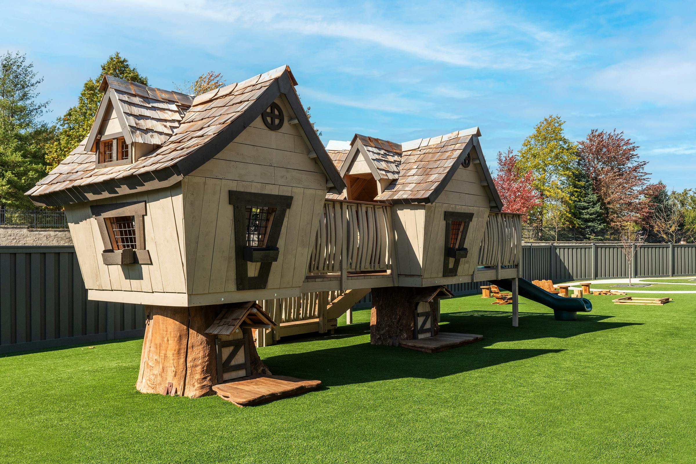 Two wooden playhouses connected by a bridge on a green lawn