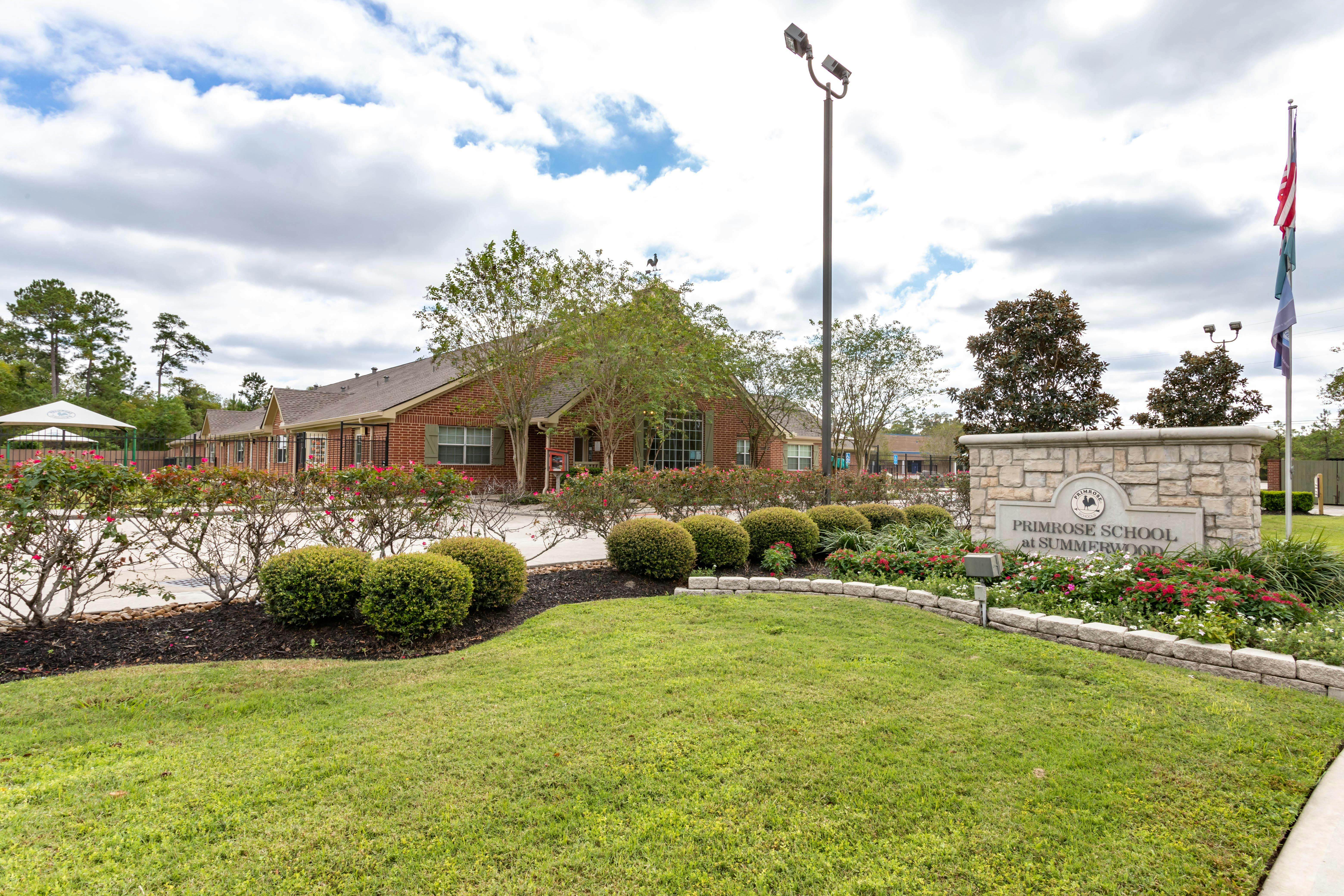 Brick building behind a green lawn and a stone sign for Primrose School at Summerwood