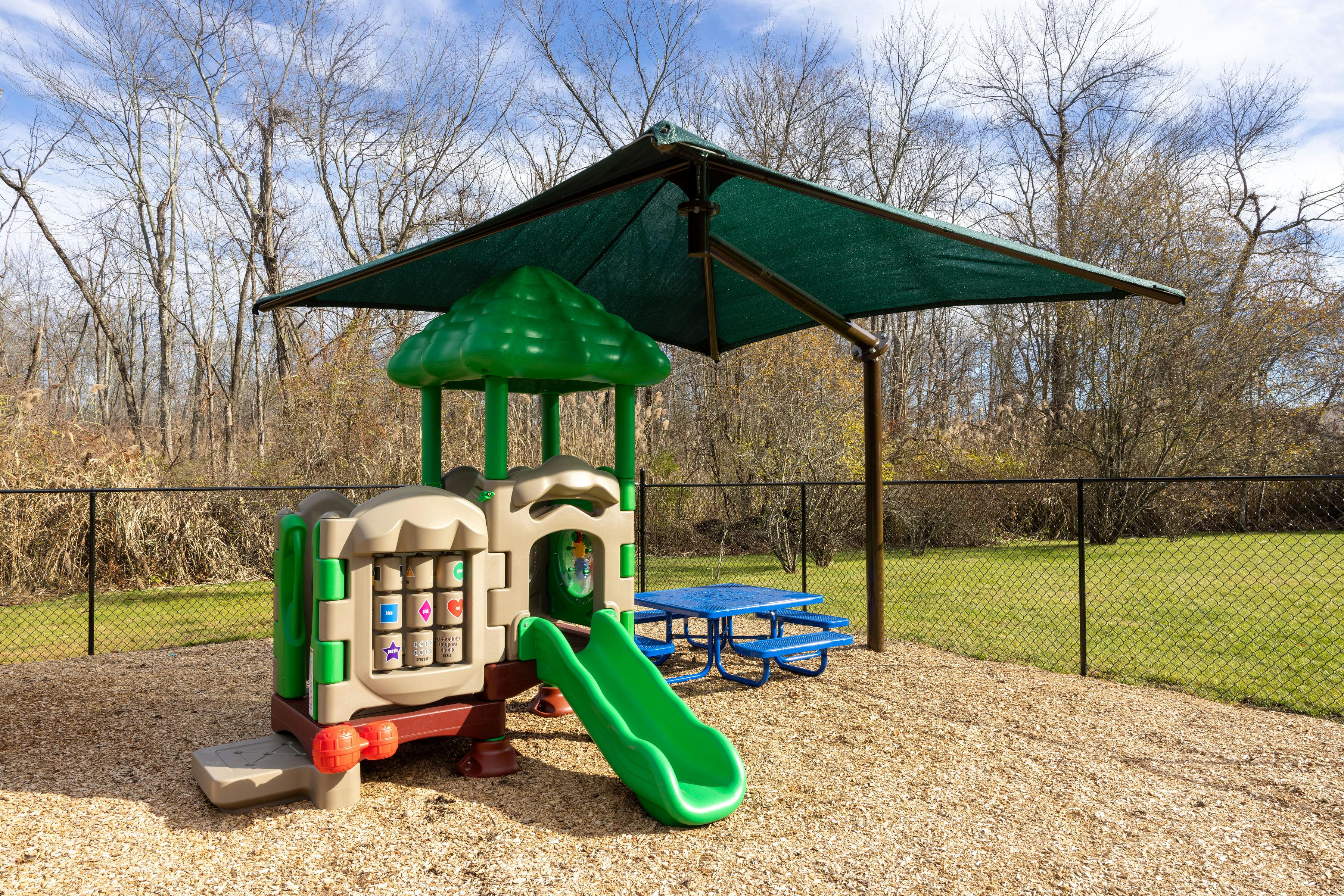 Small outdoor play structure with a slide, covered by a green shade