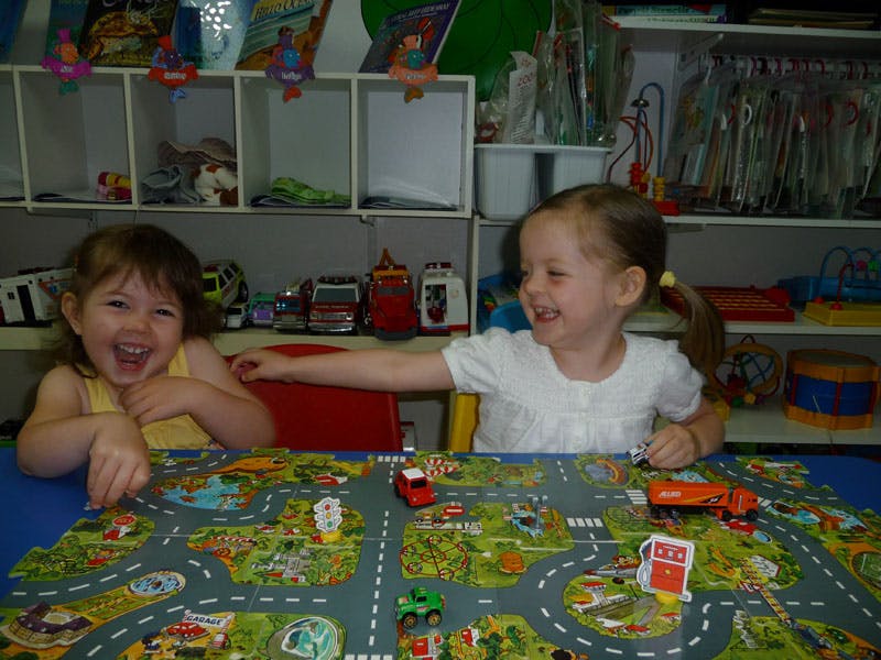 Two children playing with toy cars on a road map mat