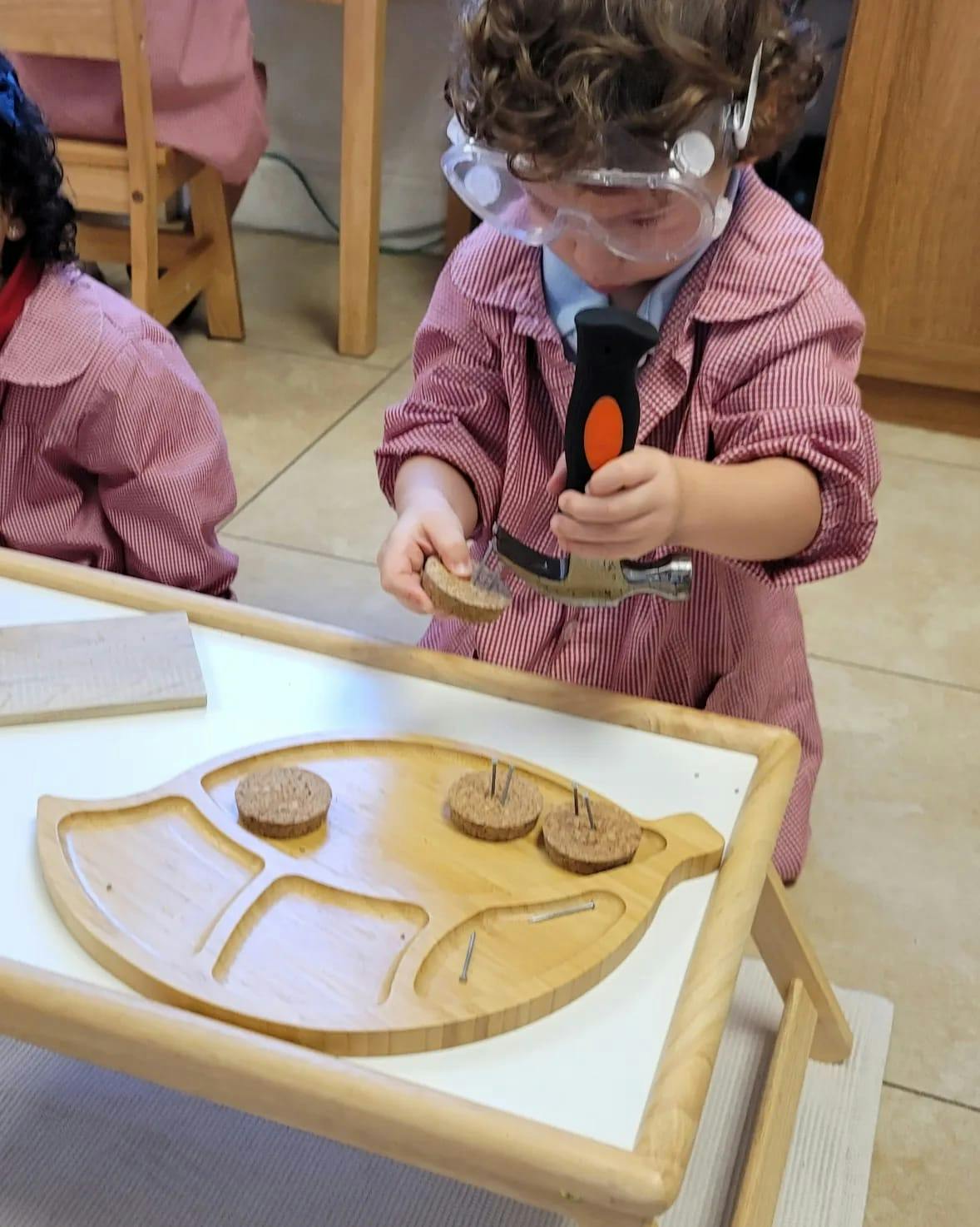 Child in safety goggles hammering a cork into a wooden board