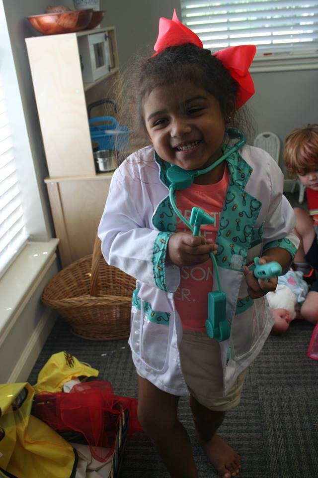 Child in a doctor's coat holding a toy stethoscope