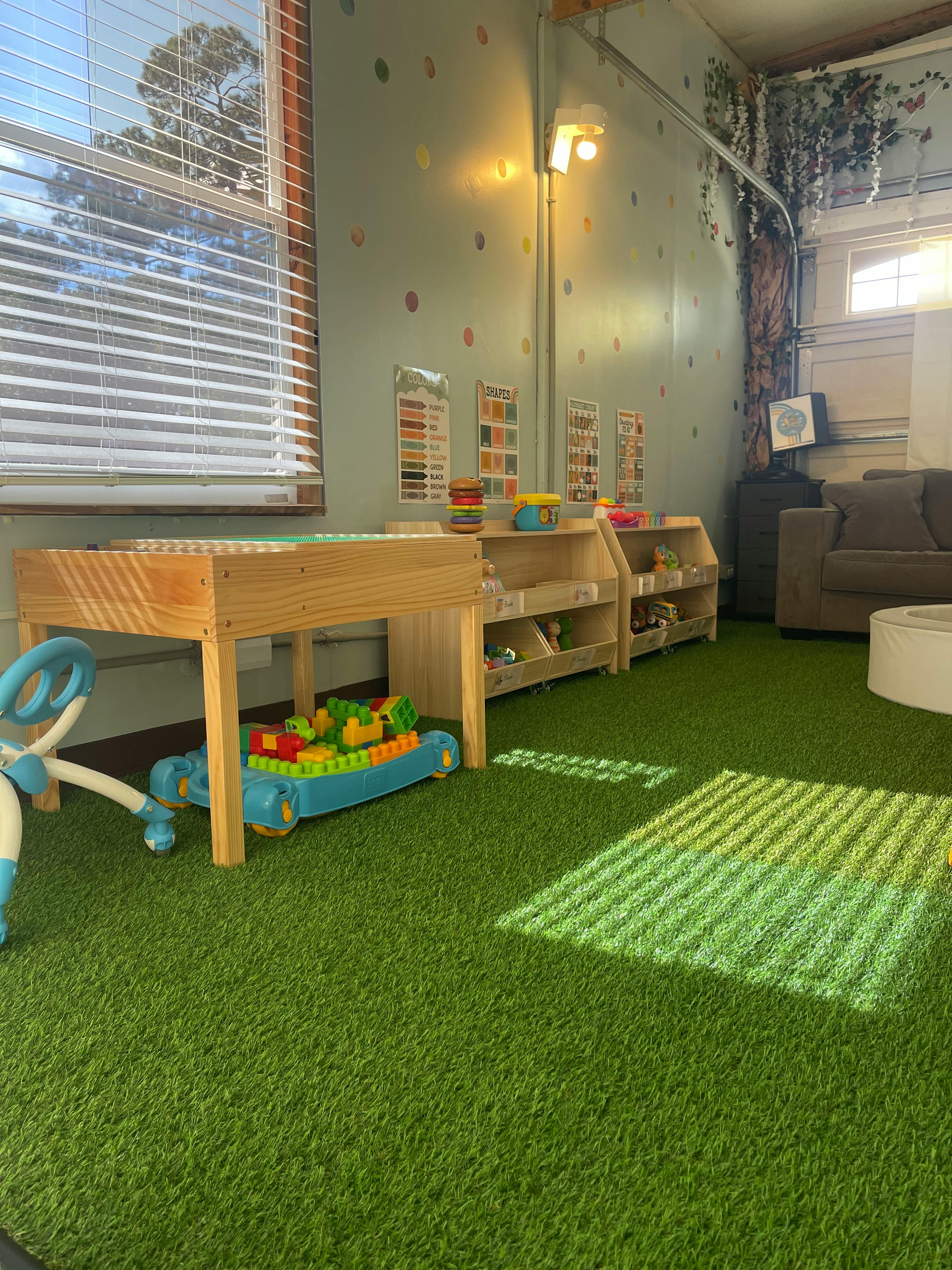 Playroom with artificial grass flooring, shelves, and various toys