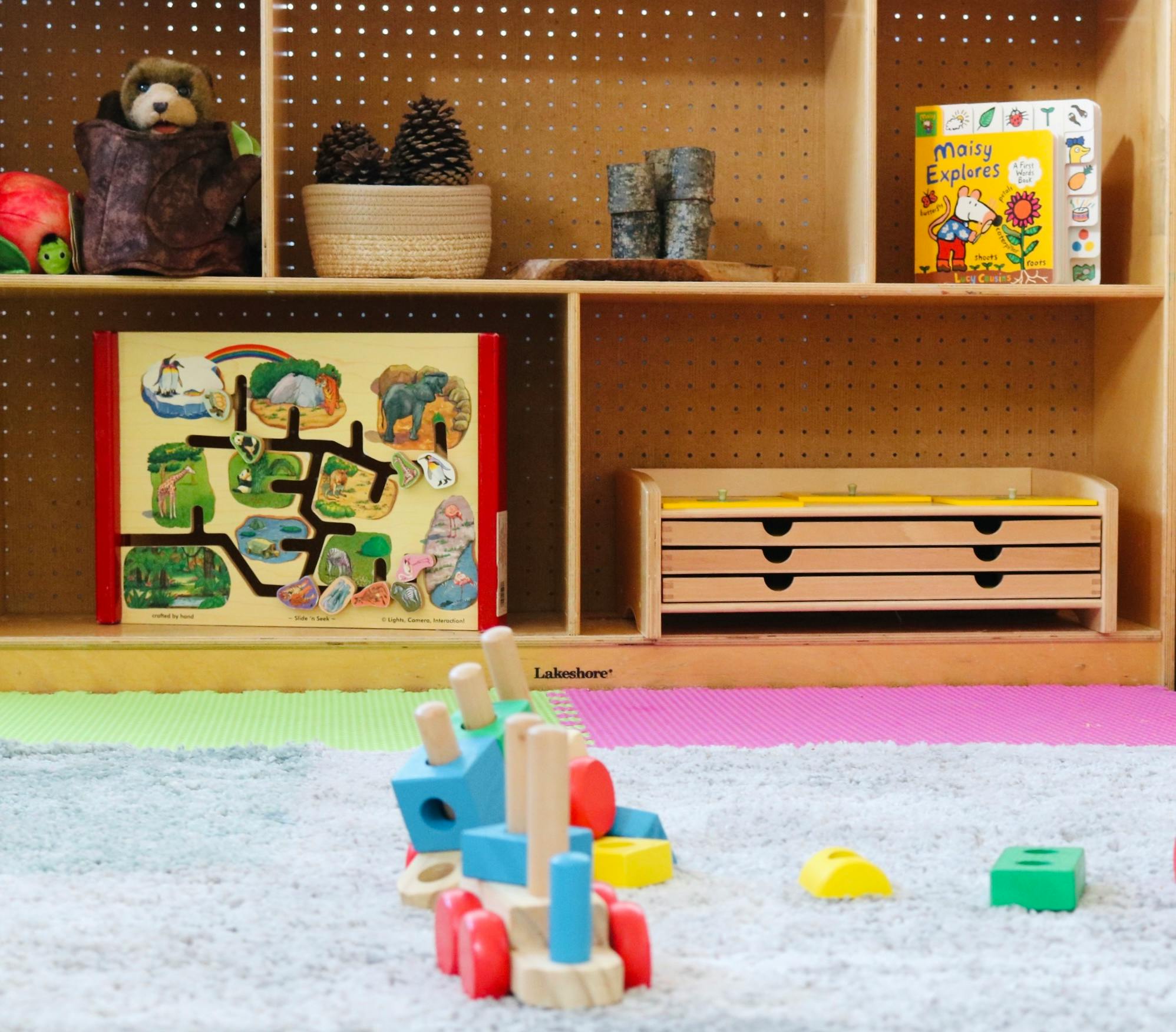Wooden toy shelf with books and puzzles and a stackable toy on a rug