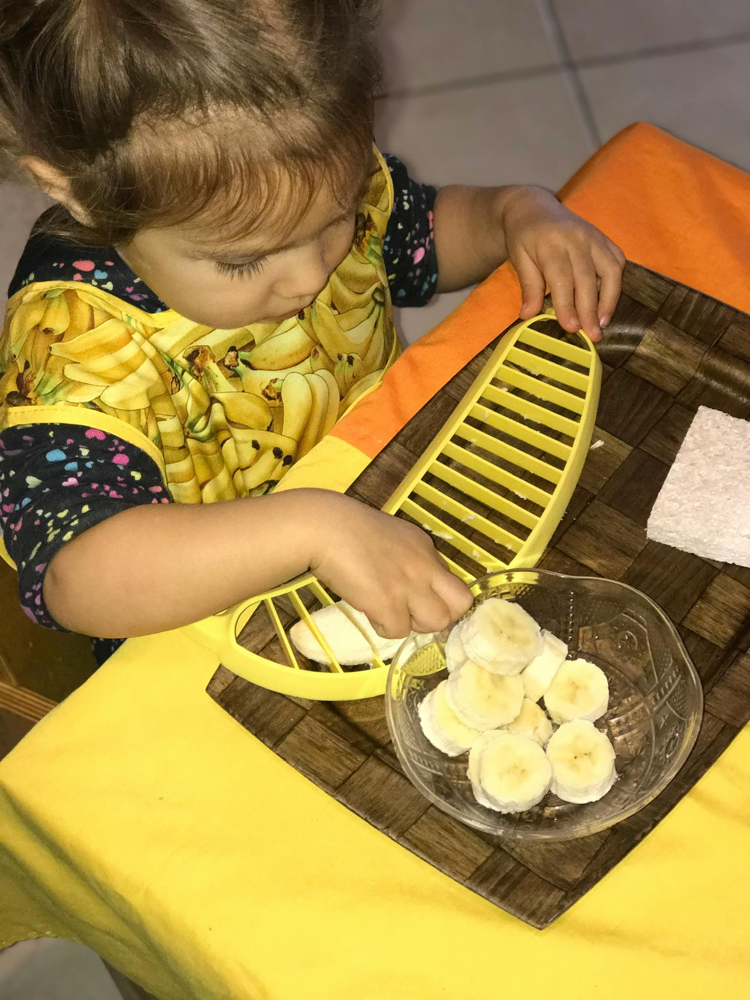 Child using a banana slicer to prepare sliced bananas in a bowl