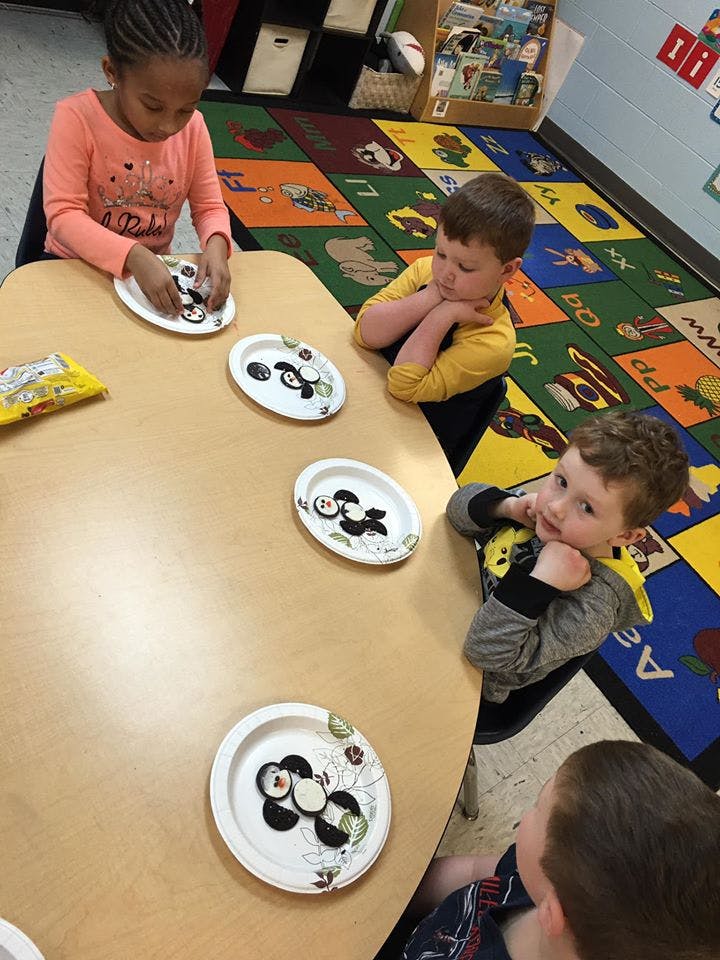 Child assembling craft on paper plate at a table with other children