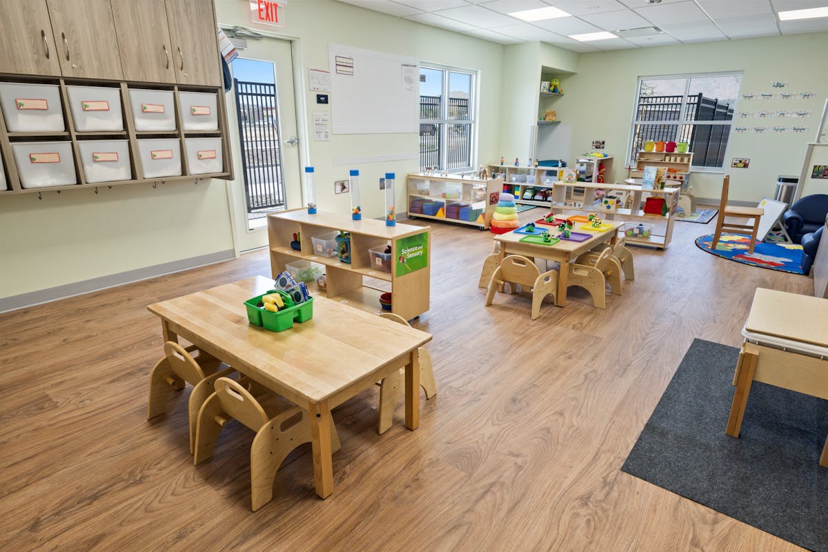 Empty classroom with small tables, chairs, and shelves full of learning materials