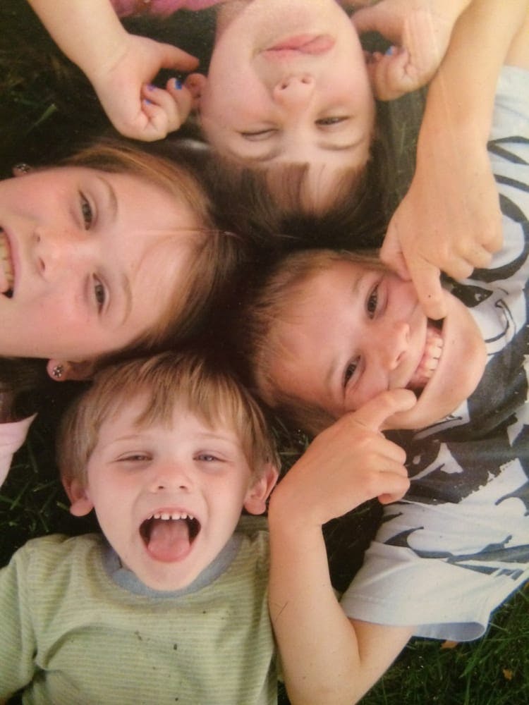 Four children lying on grass making silly faces