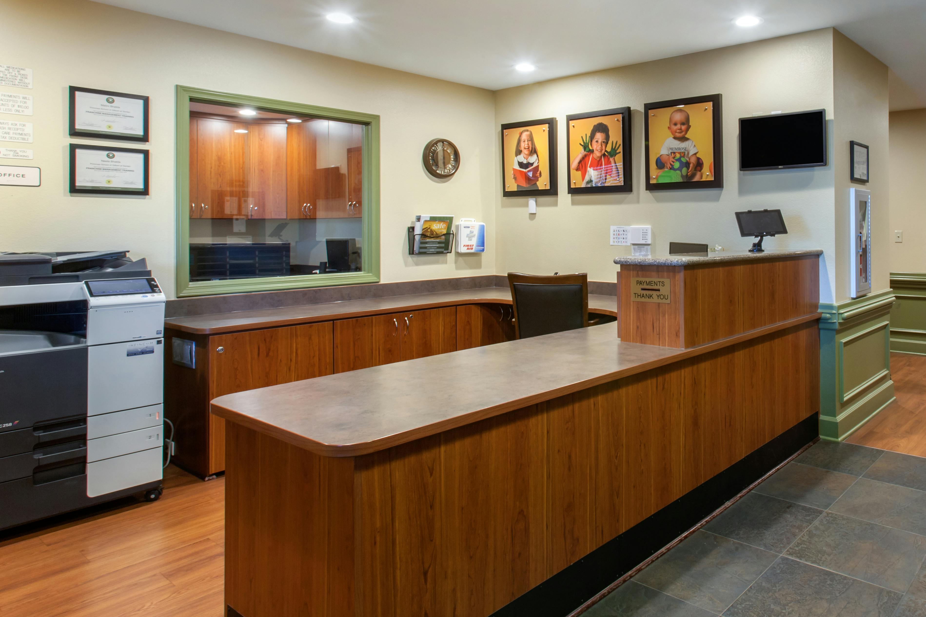 Reception desk with office equipment and framed photos of children on the wall