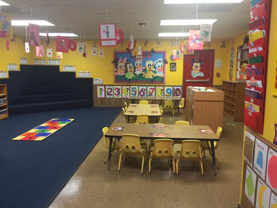 Empty classroom with small tables and chairs, and a carpeted area with steps