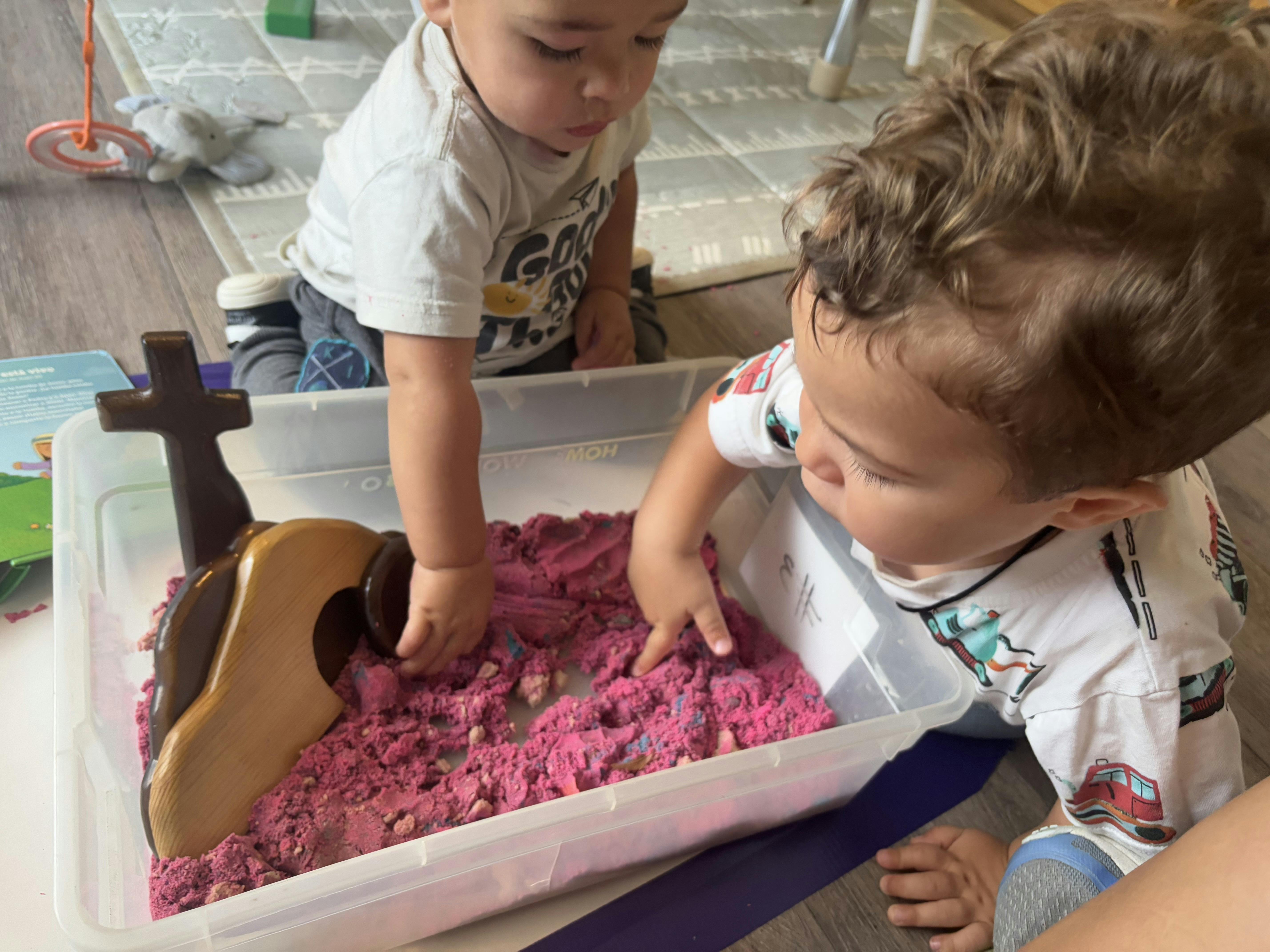 Two young children playing with kinetic sand in a clear bin