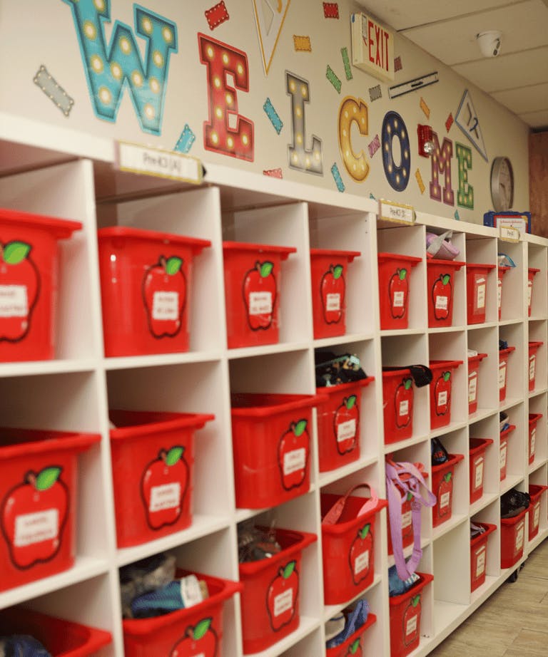 Cubby shelving with red bins in a classroom, "Welcome" sign on the wall