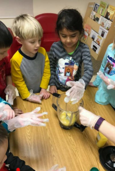 Children wearing gloves around a blender on a table