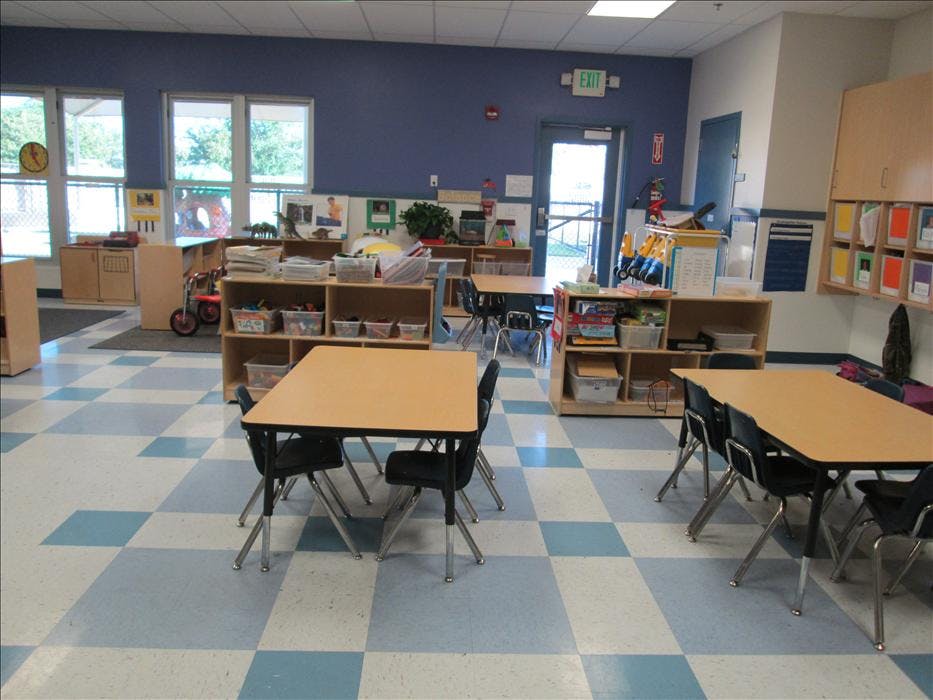 Classroom with small tables and chairs, shelves with toys, and blue checkered floor