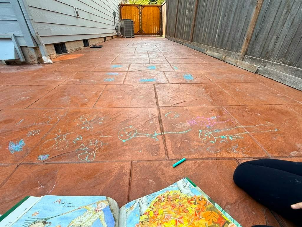 Child drawing with chalk on a patio next to an open book