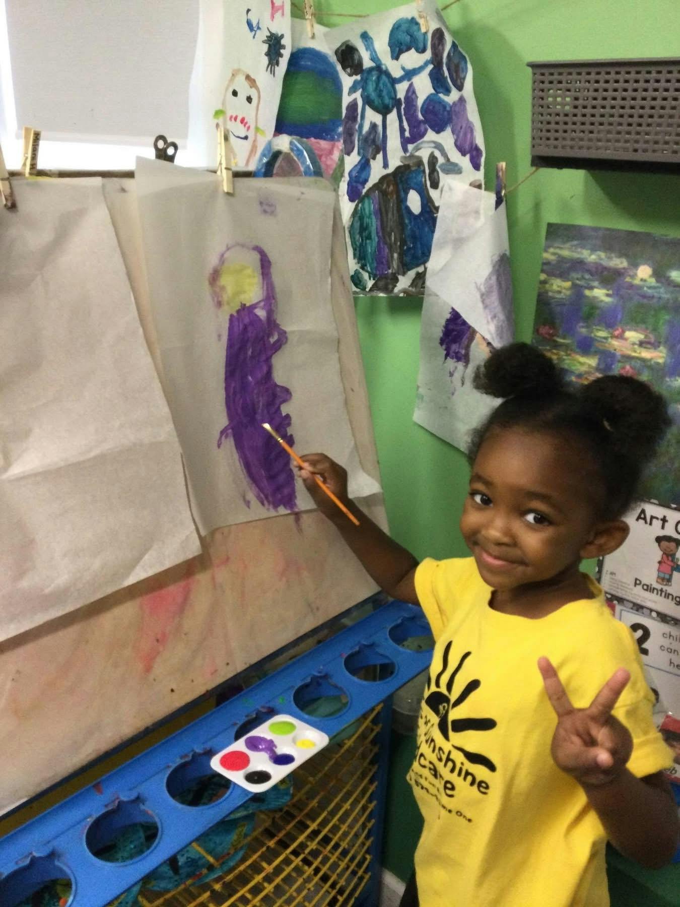 Child painting on an easel, holding up a peace sign