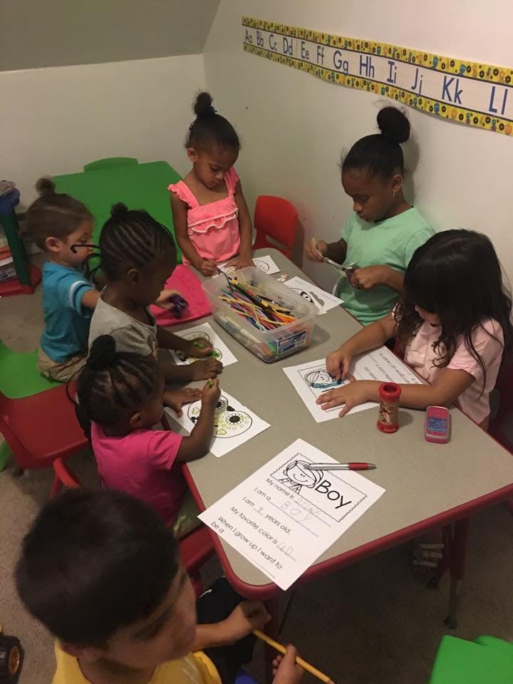 Children sitting at a table coloring and cutting paper