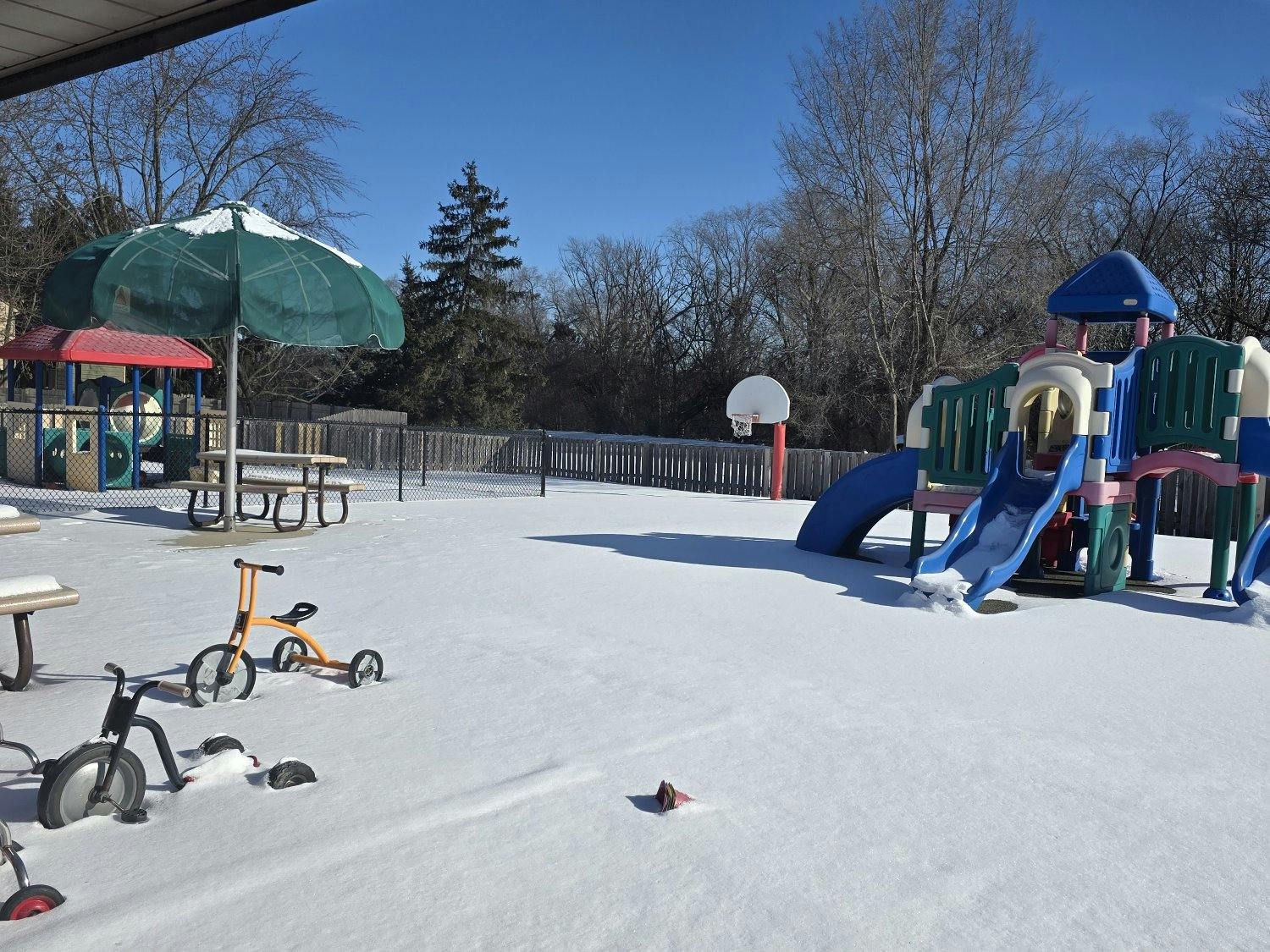 A snow-covered playground with tricycles and play structures