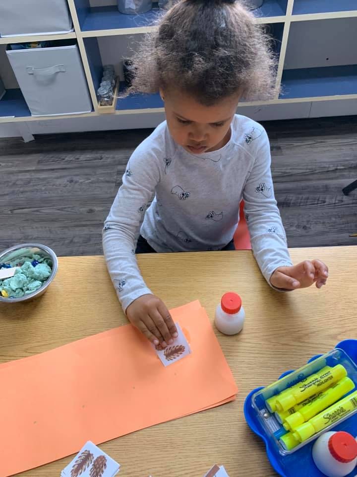 Child applying a sticker to orange paper at a table