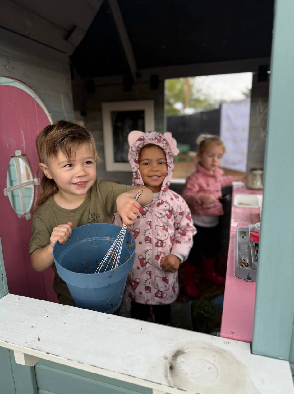 Child mixing in a bucket with a whisk next to another child