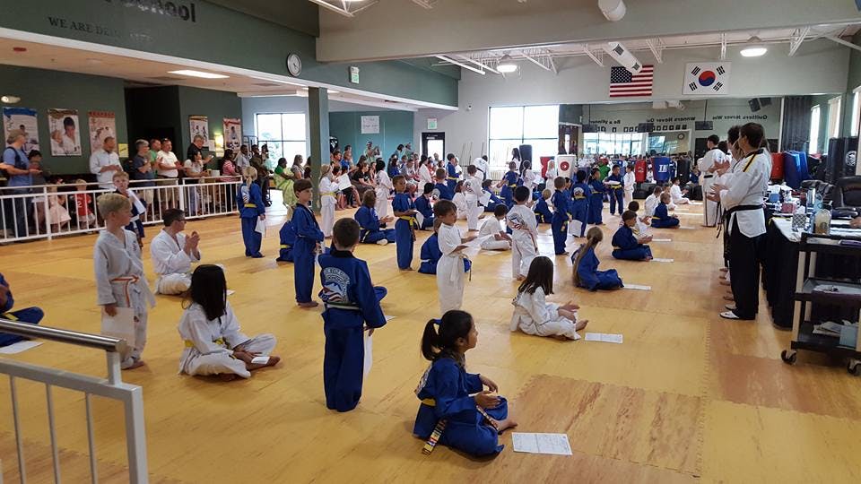 Many children in martial arts uniforms in a large room with adults watching