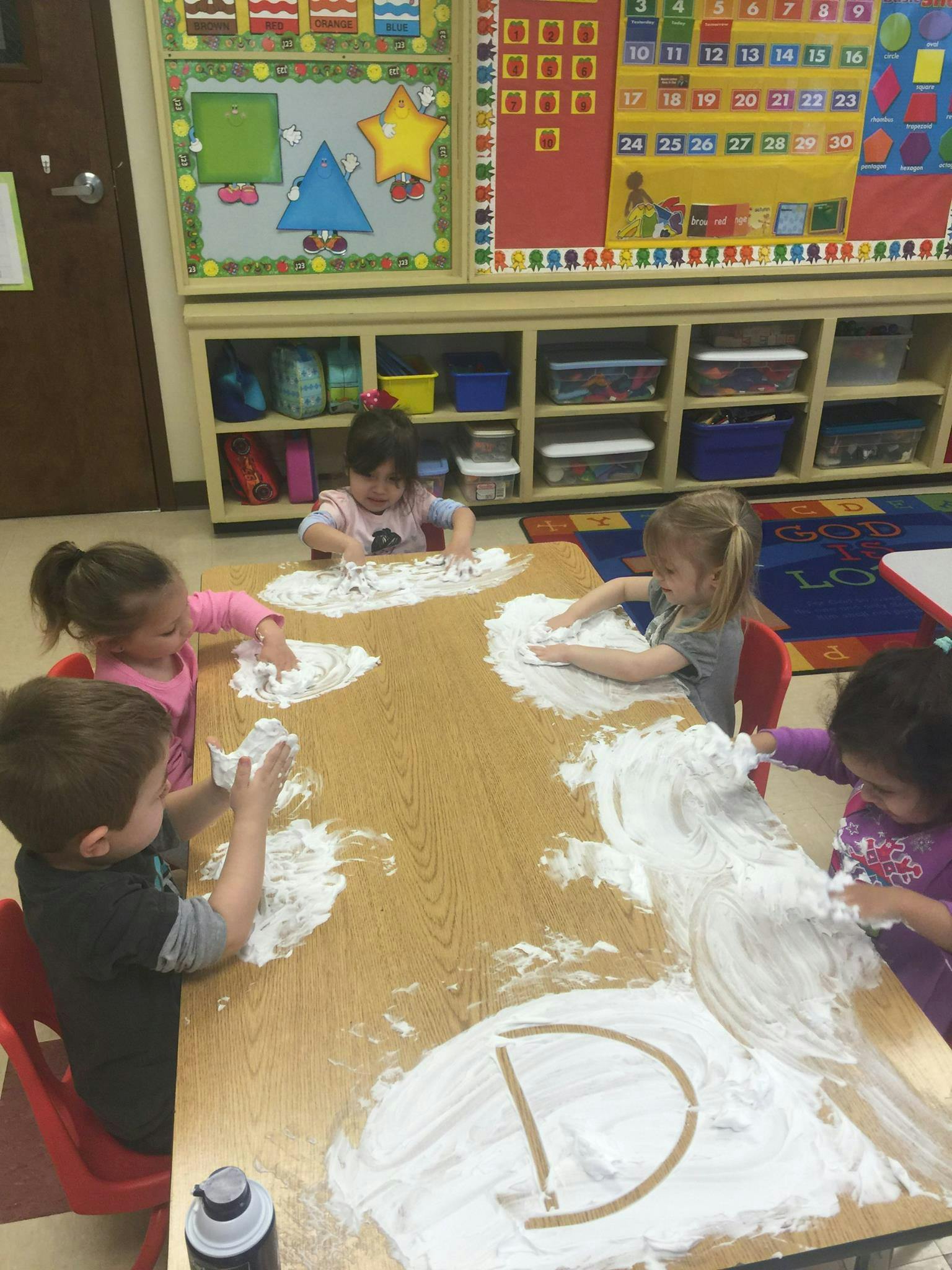Children playing with shaving cream on a table in a classroom