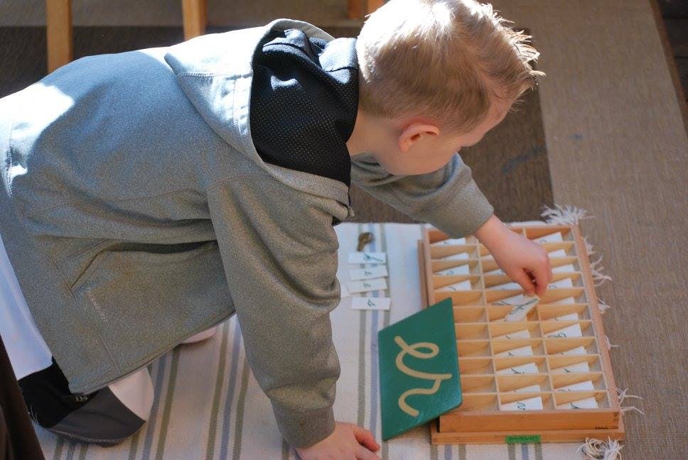 Child kneeling and reaching into a wooden box with small compartments