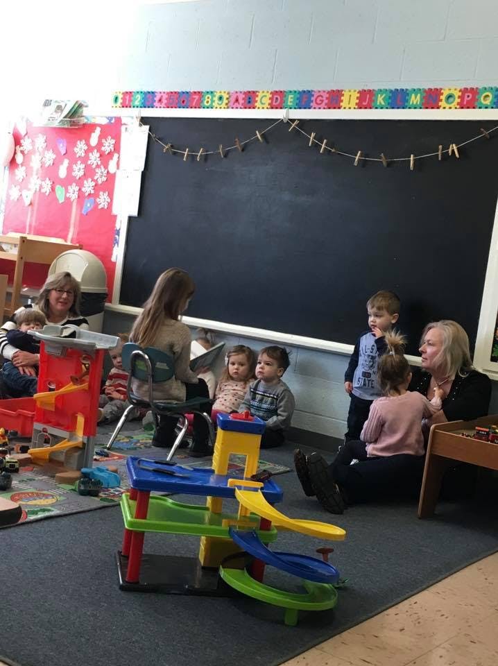 Adults and children gathered in a classroom with toys