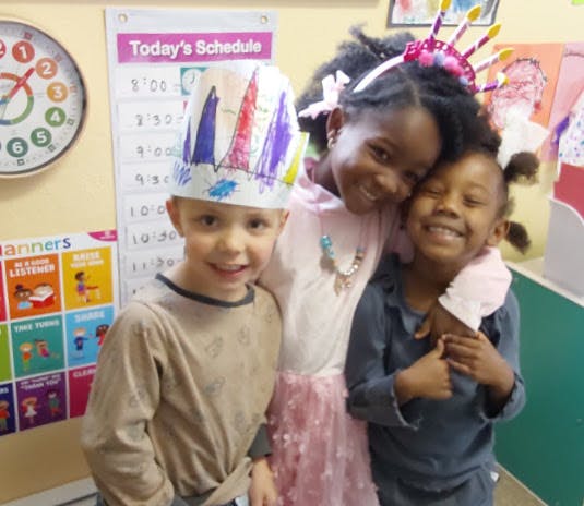 Three children smiling, one wearing a paper crown