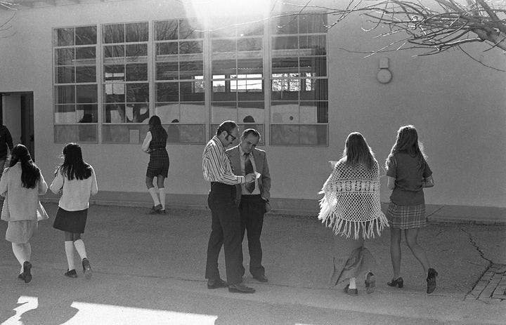 Two men talking in a courtyard while several teens walk nearby