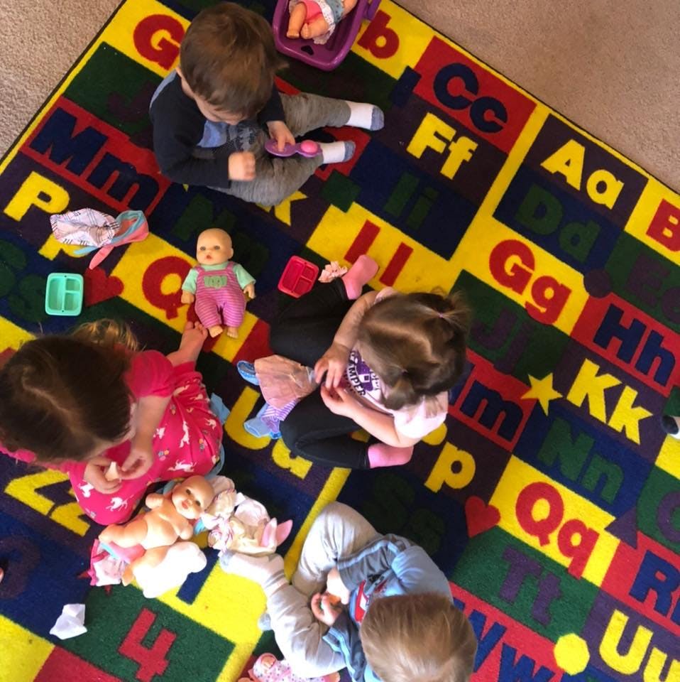 Children playing with dolls and toys on an alphabet rug