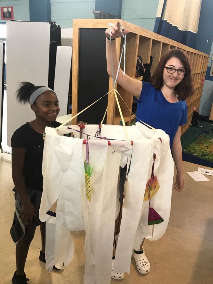 Person holding a hanging craft with a child standing nearby