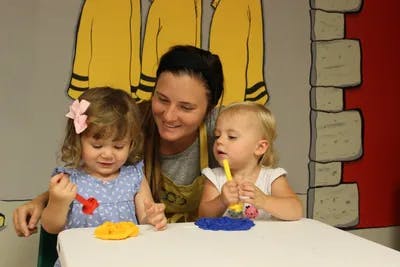 Person with two children playing with colorful objects at a table